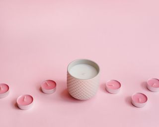 A large glass candle with assortment of pink tealight candles on pink background