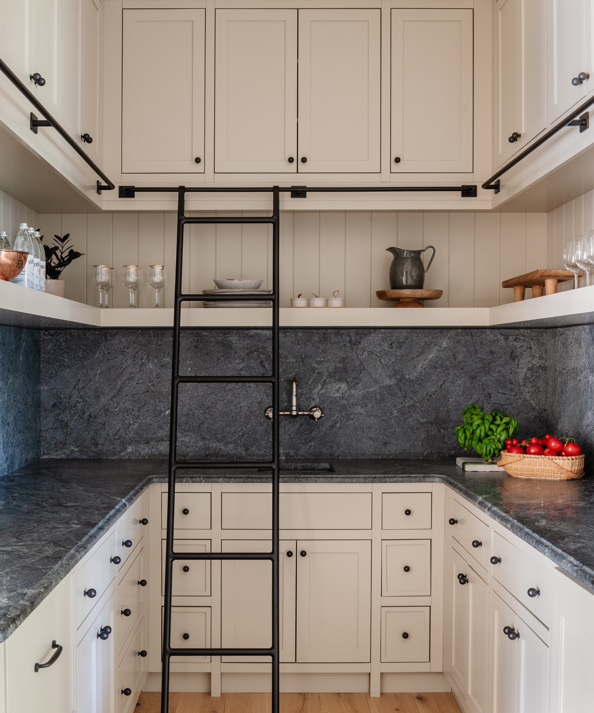 A neutral walk-in pantry painted in Farrow &amp;amp; Ball's Dropcloth, with black hardware and a dark countersplash providing depth and contrast