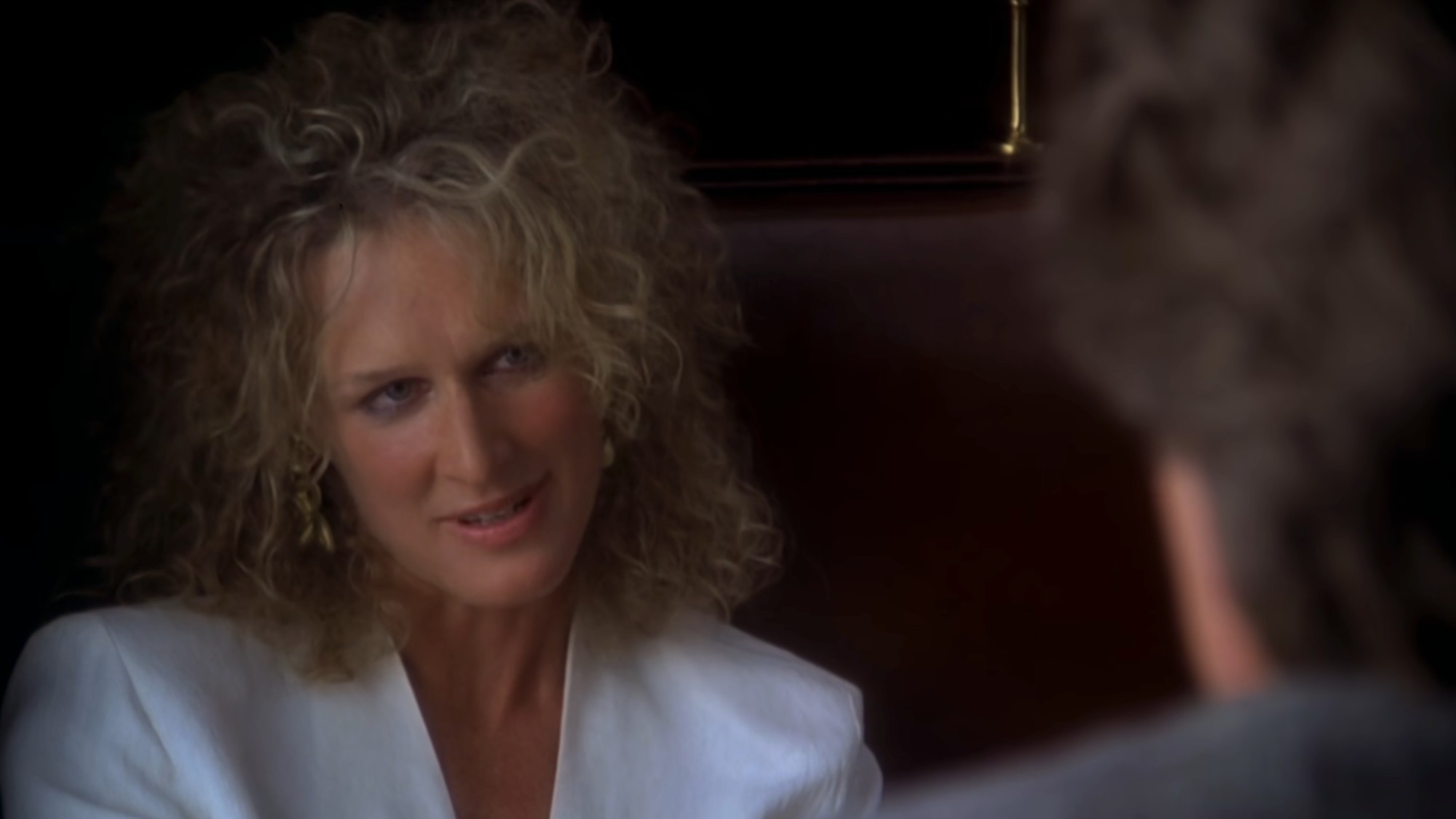Glenn Close in a white jacket, sitting in a booth in Fatal Attraction