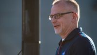 a man wearing a dark nasa logo polo shirt and glasses smiles with a greying goatee.