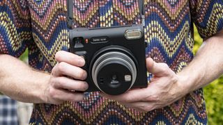 Fujifilm Instax SQ40 holdes i hendene av en person med fargerik skjorte