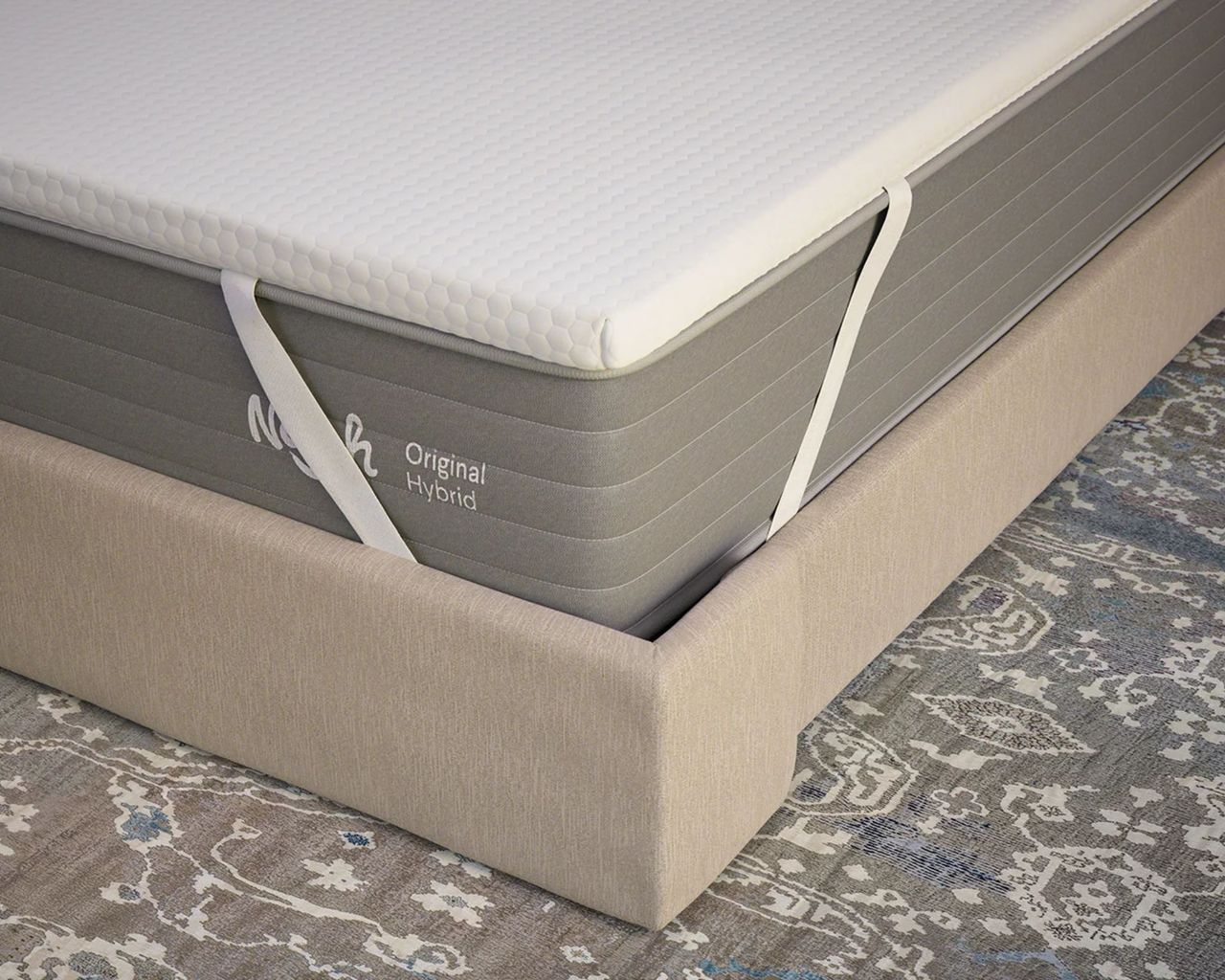 Nolah AirFoam&reg; Luxe Mattress Topper on a grey Nolah Original Hybrid mattress, shown on a beige bed frame on top of a grey patterned Persian-style rug.