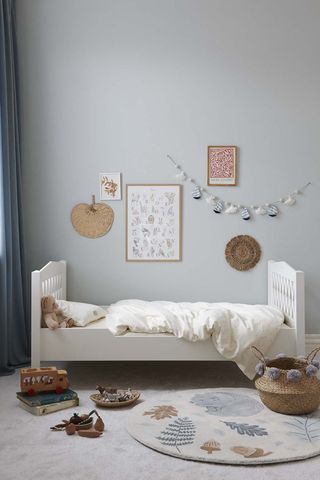 how to design a kid's room A pale blue kids room with a white bed and natural decor and prints on the wall