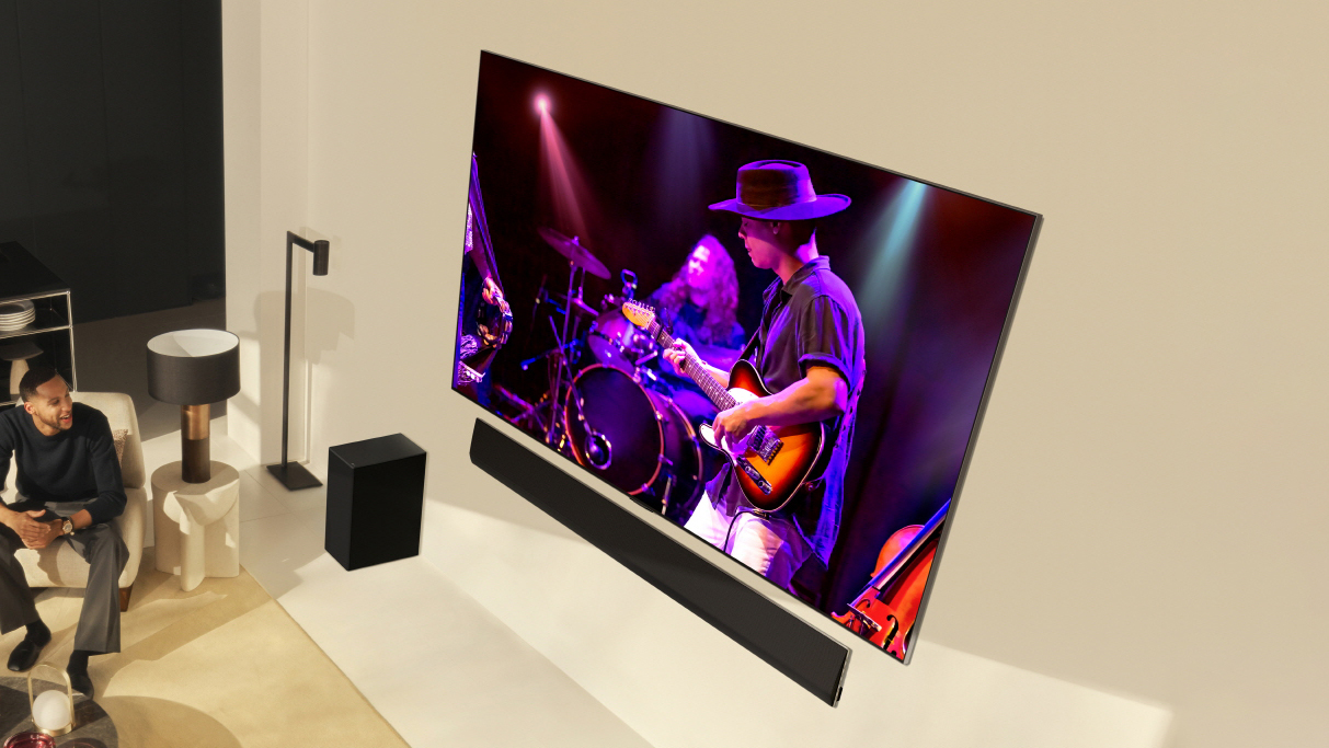 LG G4 OLED TV på beige vägg och visar ett band som spelar musik på skärmen.