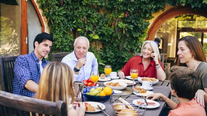 Spanish grandfather conversing with preteen granddaughter during weekend breakfast at outdoor dining table in family home.