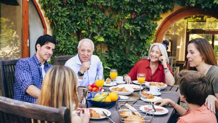 Spanish grandfather conversing with preteen granddaughter during weekend breakfast at outdoor dining table in family home.