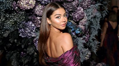 Sarah Hyland attends the Christian Siriano SS24 Runway Show at The Pierre Hotel on September 08, 2023 in New York City while wearing a purple off the shoulder dress and posing in front of a floral wall