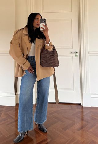 best elevated basics shown in a photo of a woman wearing a tan trench coat over a white t-shirt with jeans and black ankle boots