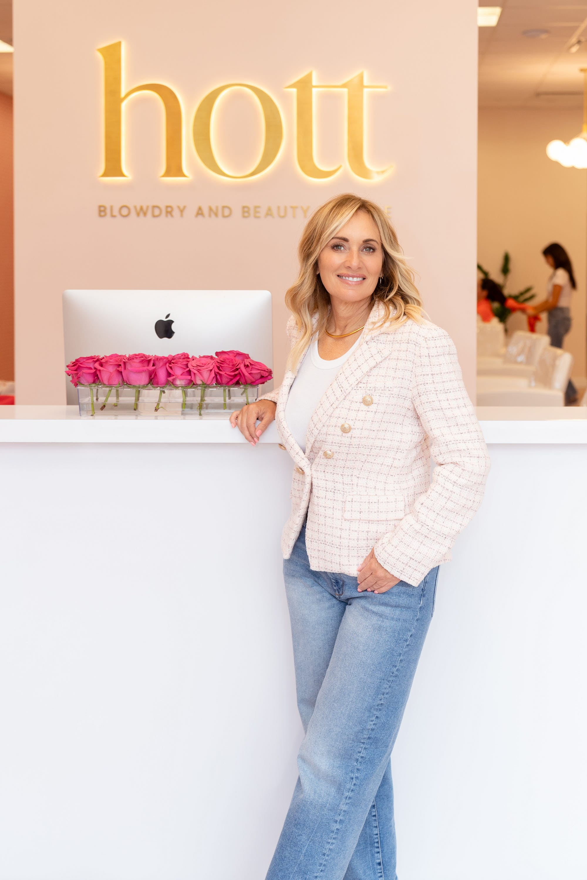 a professional headshot of a blonde woman wearing a pink and white blazer with blue jeans