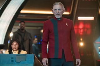 a man in a red tunic stands at the helm of a starship