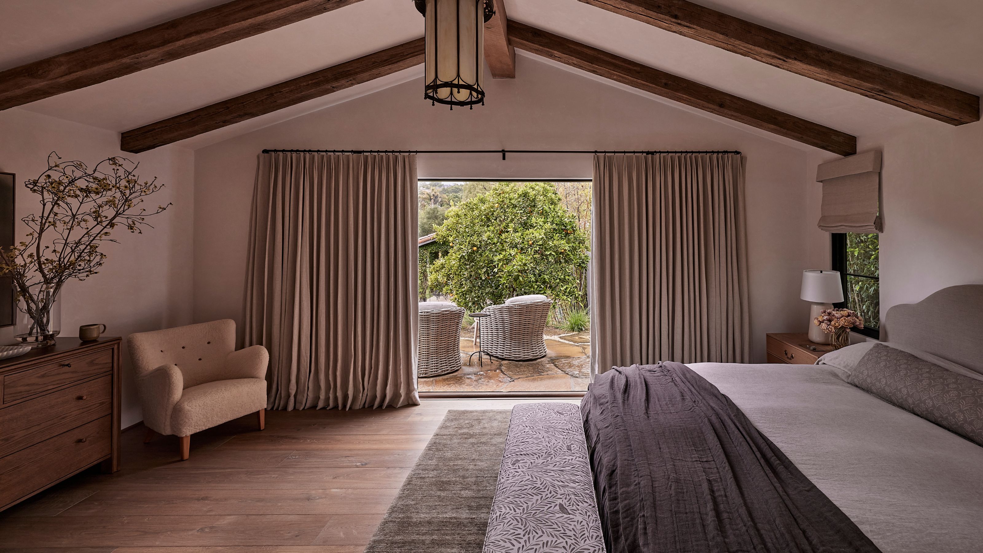 a warm soft pink primary bedroom with vaulted ceiling and soft gray upholstered bed with patio doors out to a private seating area