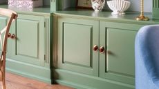 green built in cabinets with red handles with brass backplates. a wooden dining chair and blue armchair just peek into frame