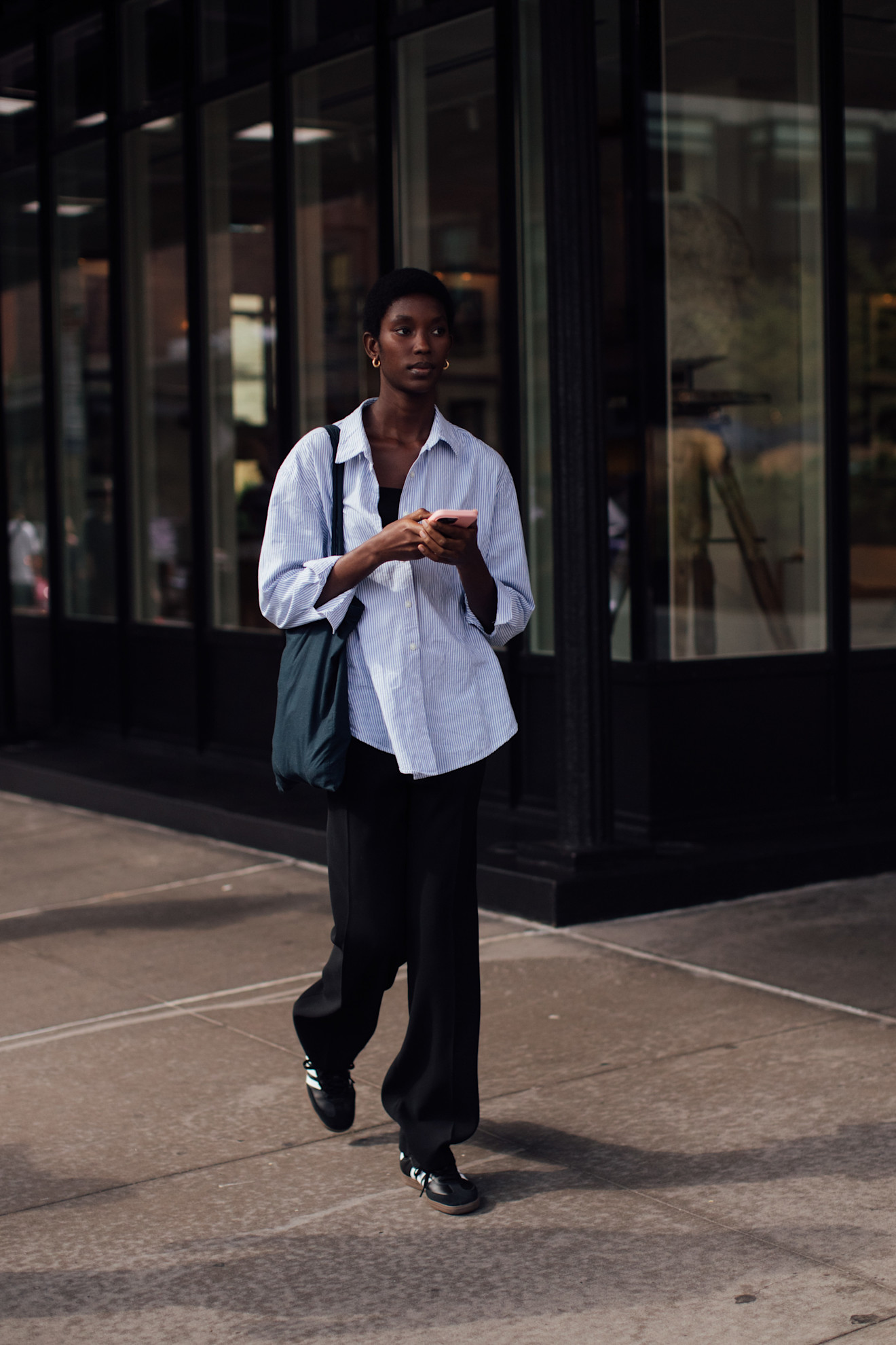 Fashion week attendee wearing striped button down shirt, black pants, adidas sneakers