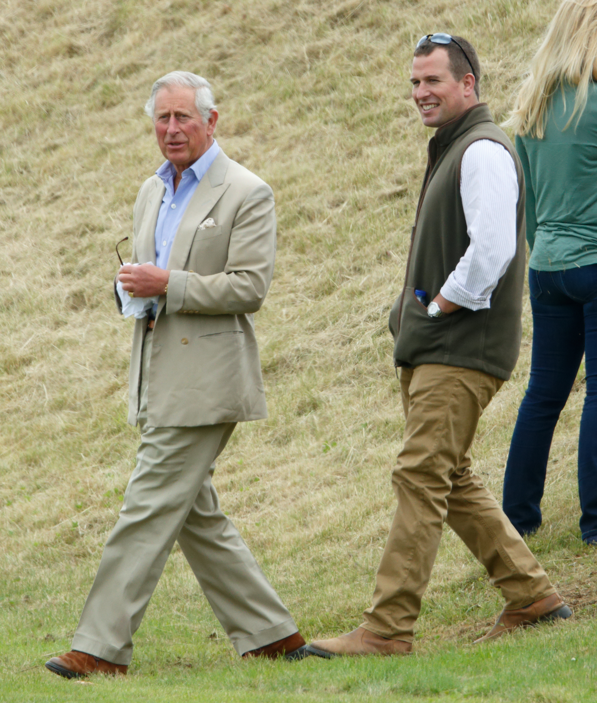 King Charles walking next to Peter Phillips across grass