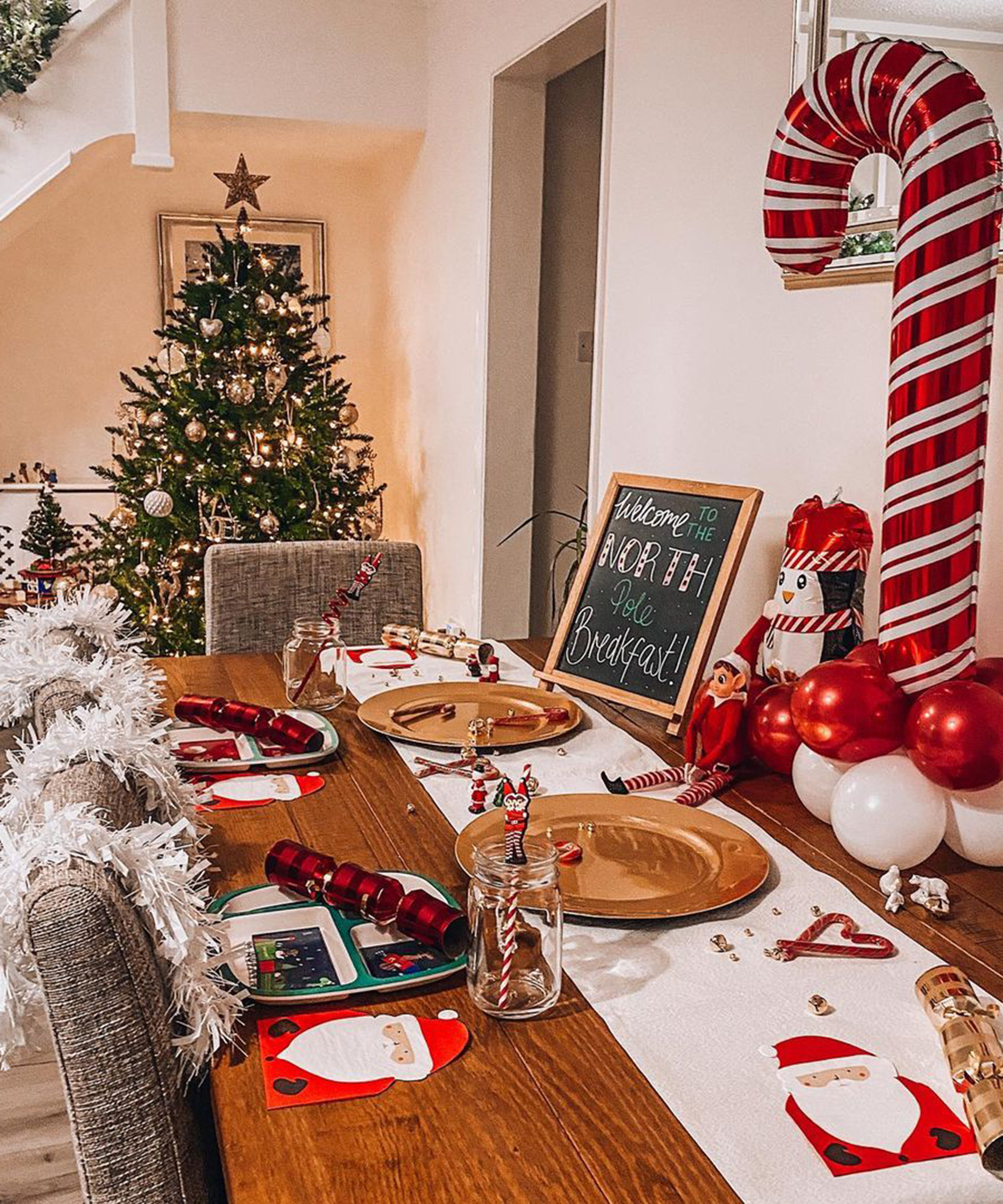 A North Pole themed table with elves and chalkboard signage on dining table with Christmas tree in background