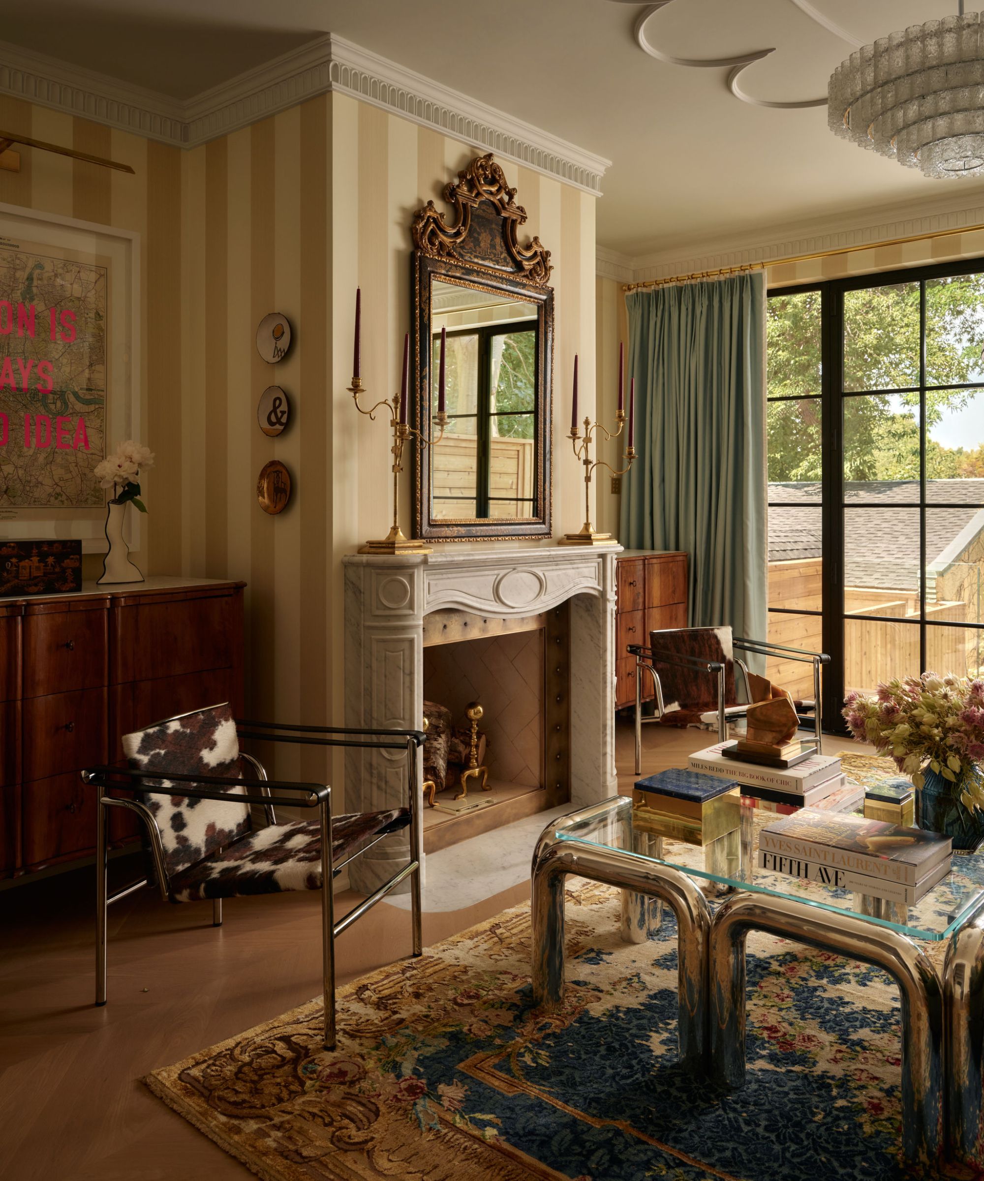 a large living room with yellow striped wallpaper, ceiling molding, vintage rug, marble fireplace, and a cow print chair
