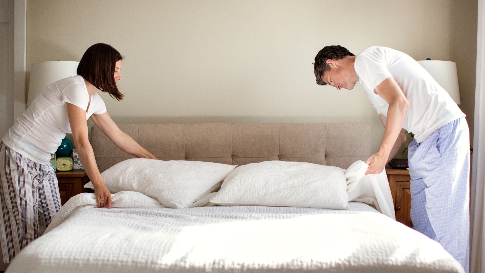 A man and a woman stand either side of a bed, adjusting the bedding.