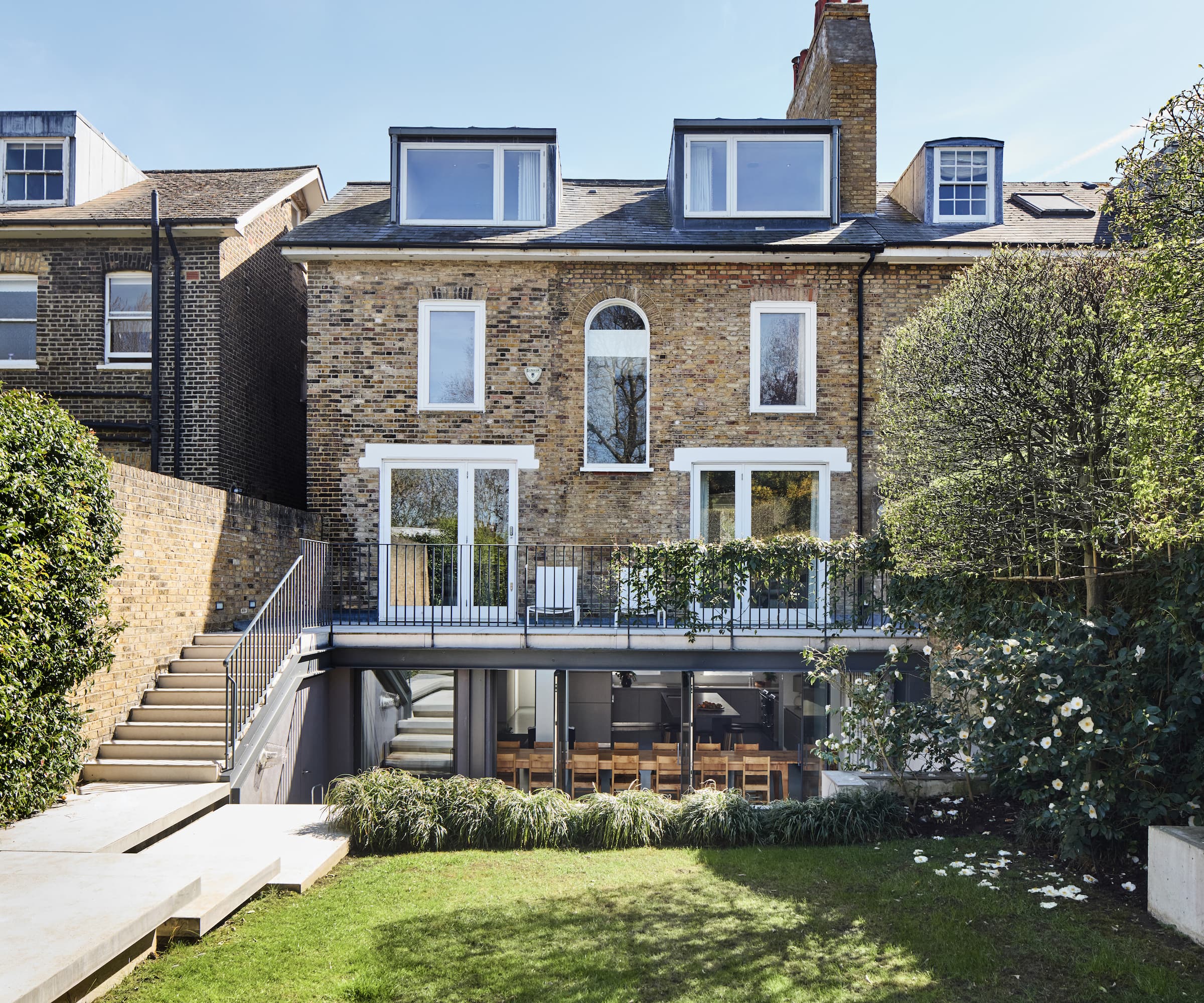 A patio with stairs seen from a rear garden with a dining area underneath