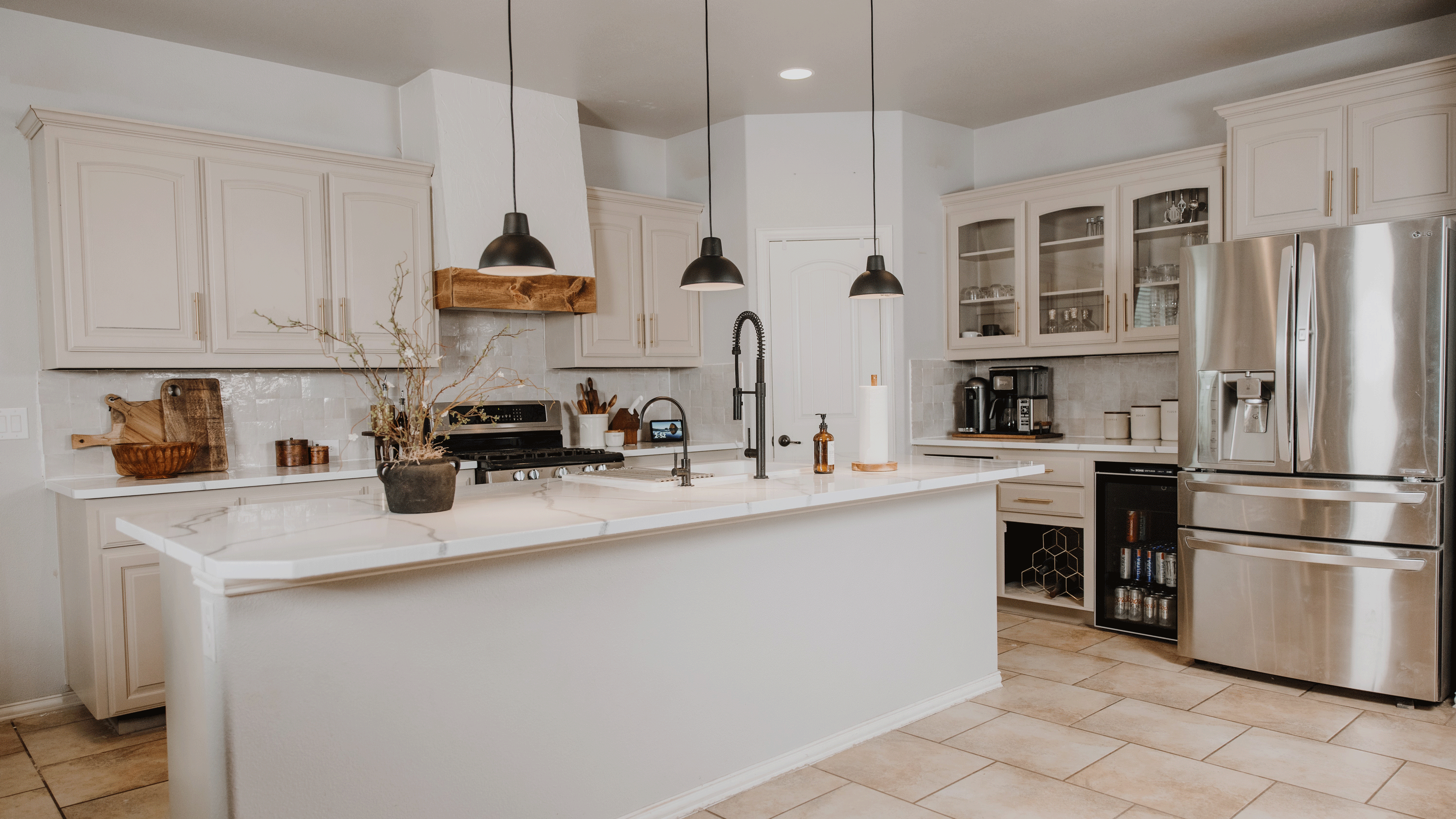 modern white and cream kitchen with large island with black hanging lights, a large stainless steel fridge-freezer, and a wooden extractor fan