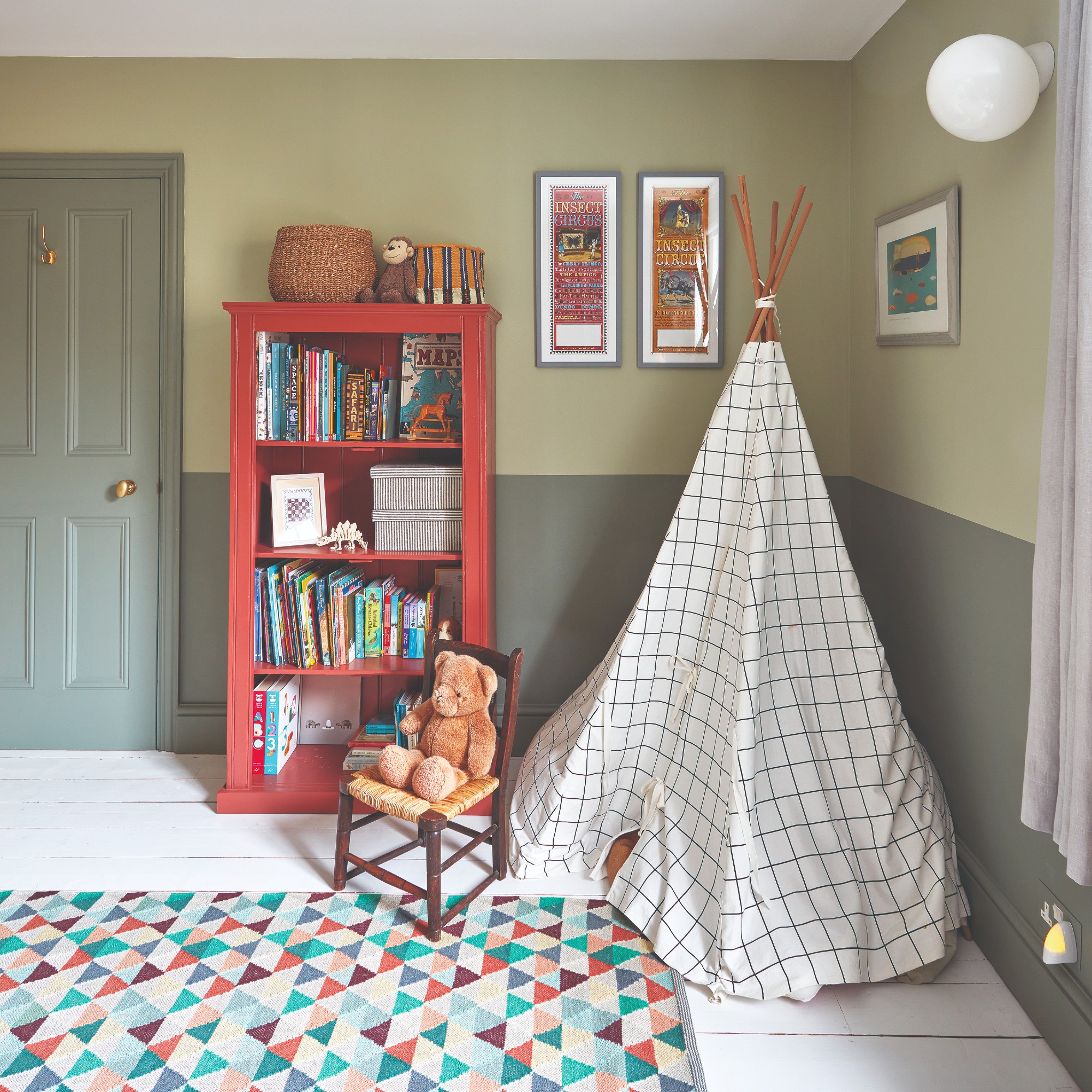 A two-tone green child's playroom with a checked teepee tent, a red bookcase and a geometric-print rug