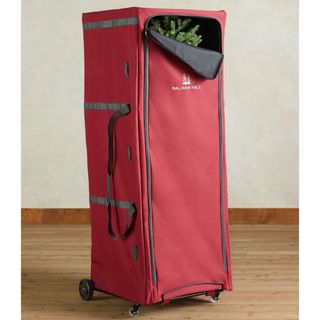 A red, upright christmas tree storage bag on wheels. Zip front, partially open showing a folded artificial tree inside