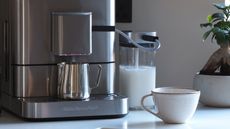 a coffee machine close up with a mug, a milk jug and a tree in the background