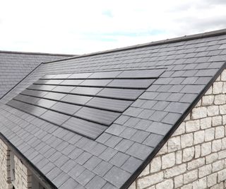 solar panels on black slate roof with cloudy sky in background