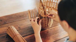 A lady weaves a wicker basket by hand