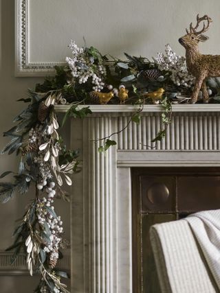 white berry style Christmas garland on mantel with three gold birds and reindeer