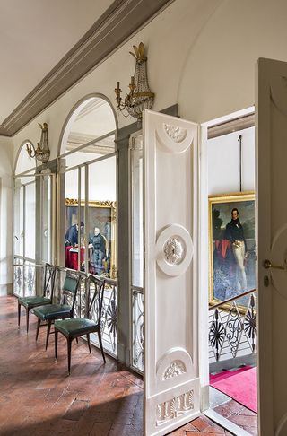 Upper floor featuring parquet flooring, three green chairs, chandelier-style wall lights and classical artwork