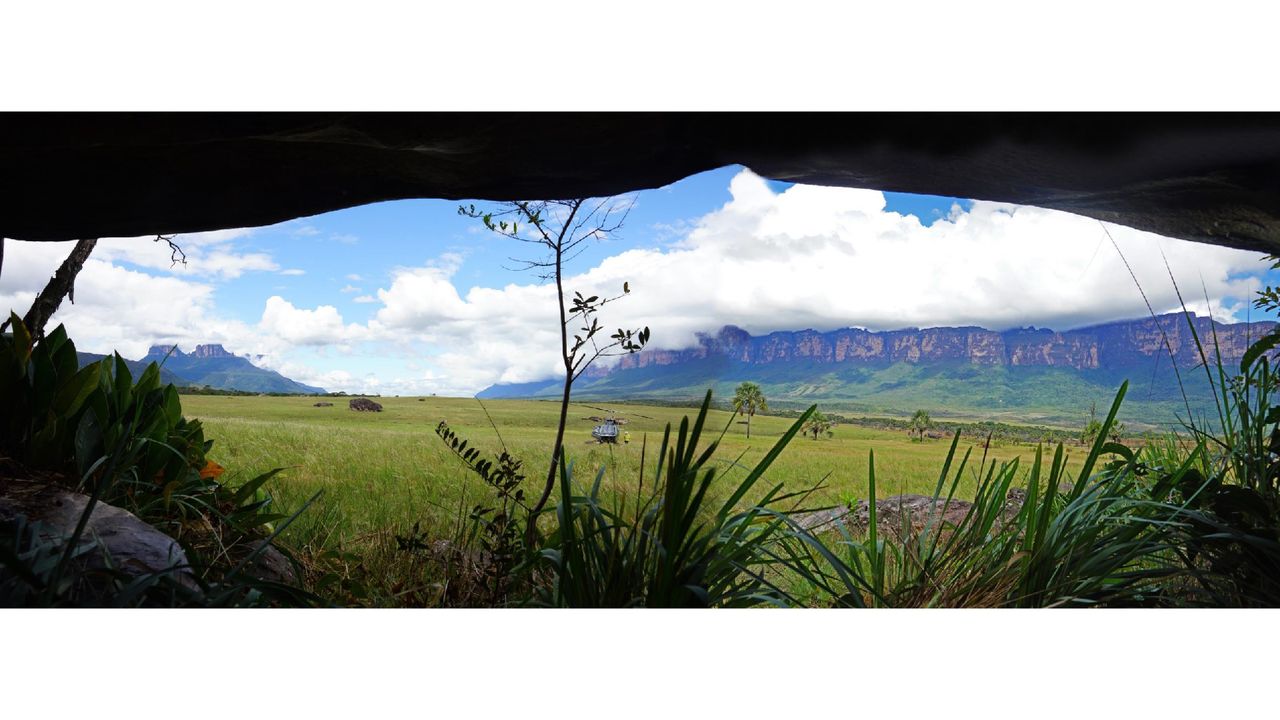 A panoramic view from inside the cave of a grassy plain with rocky mesas