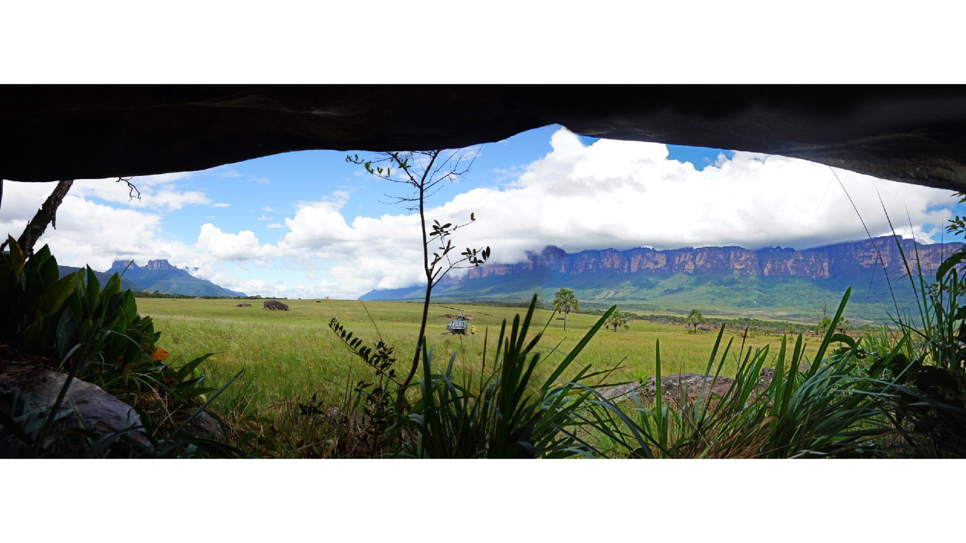 A panoramic view from inside the cave of a grassy plain with rocky mesas