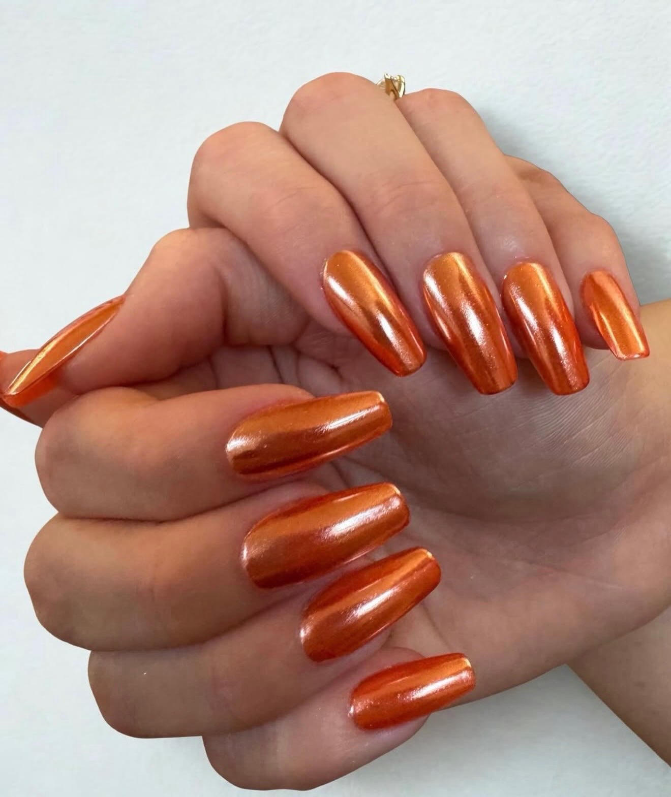 Long coffin-shaped nails painted a shiny burnt-orange chrome