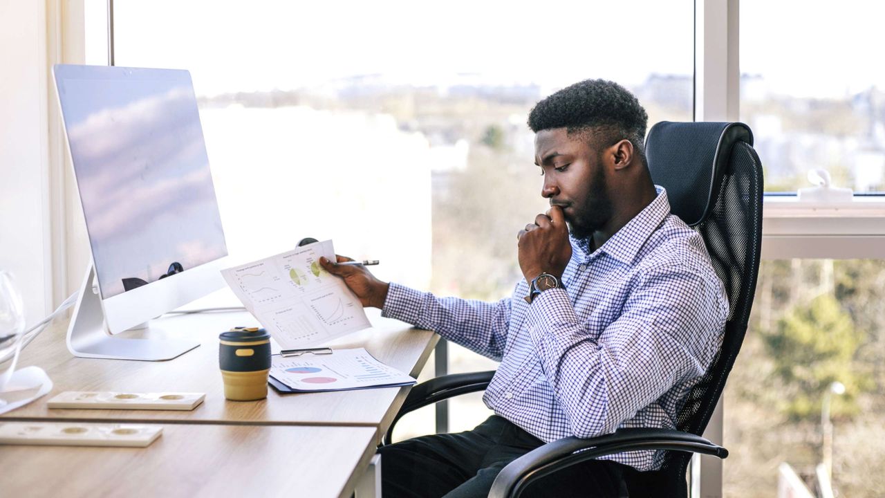 A man sits at a desk and looks at investment documents.