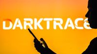 Darktrace logo pictured in the background of a silhouetted woman holding a mobile phone.