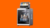 A 3D printer sits on an orange background. 