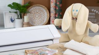 The best Cricut alternatives; a photo of a Cameo 4 Pro craft machine on a table with materials and a soft toy