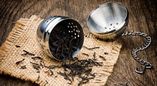 Metal tea infuser on it's side with tea leaves spilling out