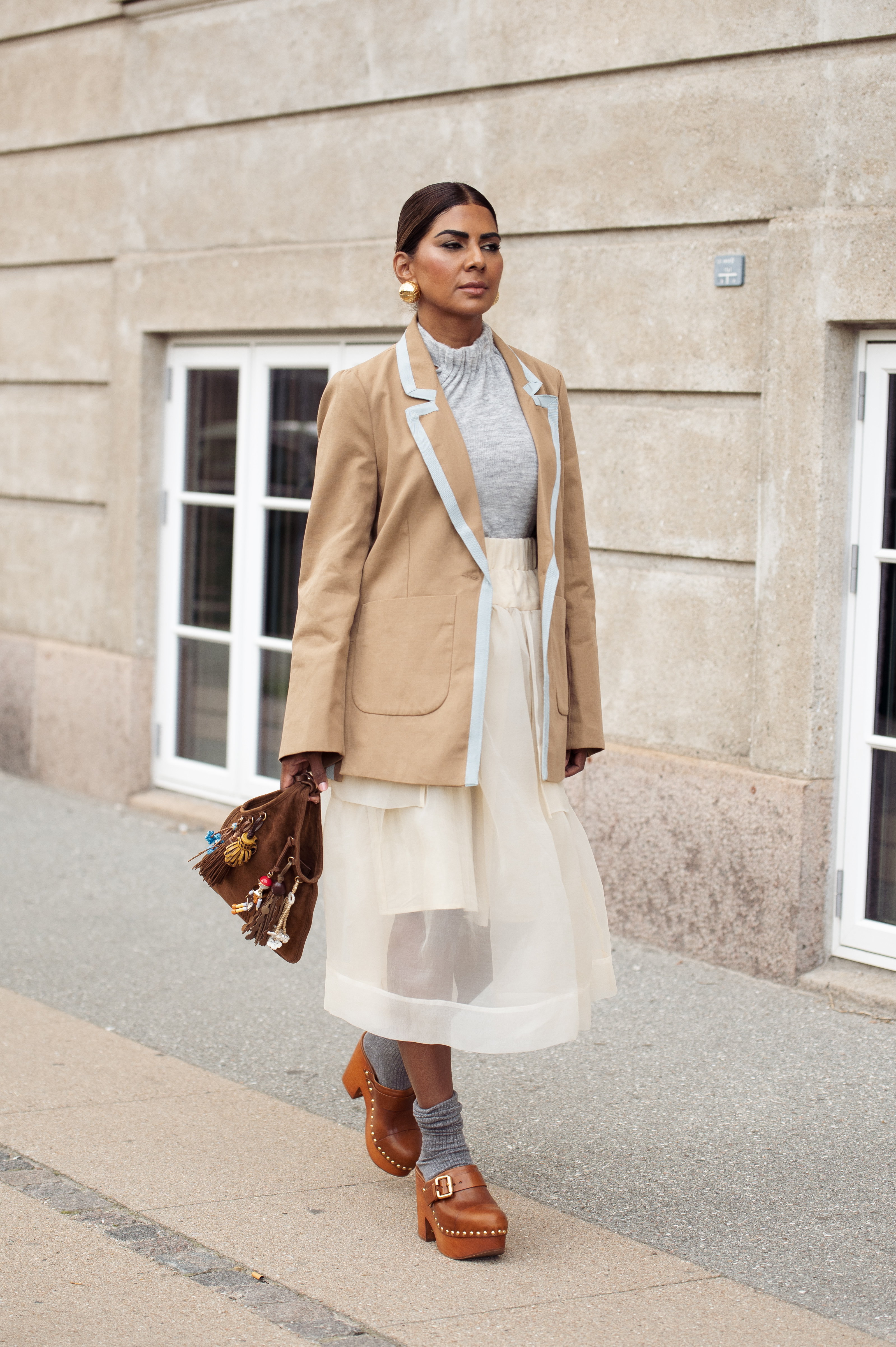 Zufi Alexander at Copenhagen Fashion Week in August 2025 wearing a white sheer skirt, a gray top, a brown suede blazer, and leather clog mules.
