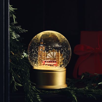 M&S Light Up London Snow Globe in the dark next to a Christmas garland and a red wrapped present