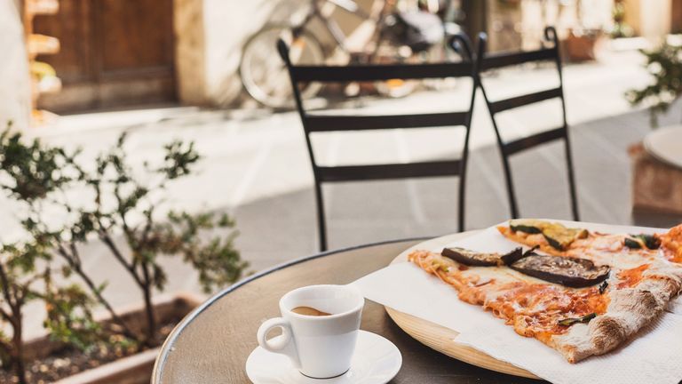 Traditional Italian dishes of pizza and coffee on top of an outdoor table in Italy