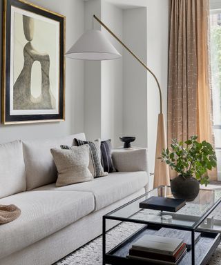 A white living room with a glass coffee table, white sofa, and large floor lamp