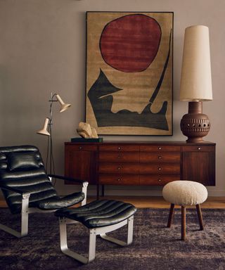 A room with a vintage leather chaise, a large wooden console table and a piece of abstract art