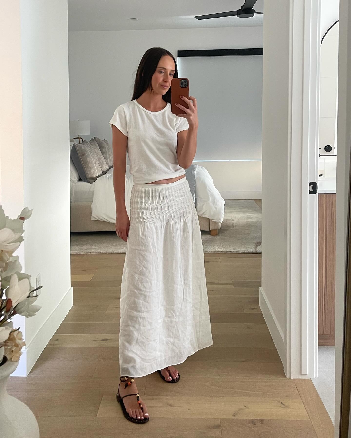 Infleuncer Makenna wears a white linen skirt, a white crewneck tee, and beaded sandals.
