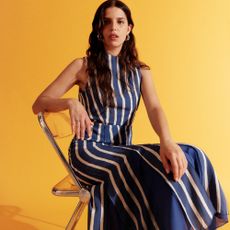 Model wearing a stripy Whistles dress sat on a chair with yellow background