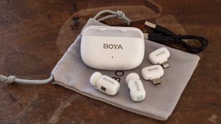 All of the Boya Mini wireless mic kit components laid out on a storage pouch on a wooden surface