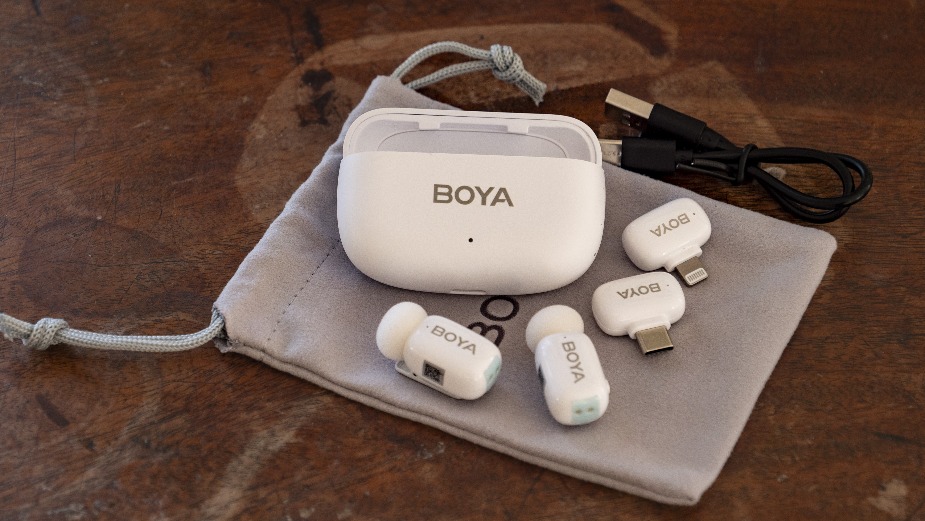 All of the Boya Mini wireless mic kit components laid out on a storage pouch on a wooden surface