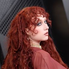 a white woman with curly red hair poses on a red carpet before an awards show