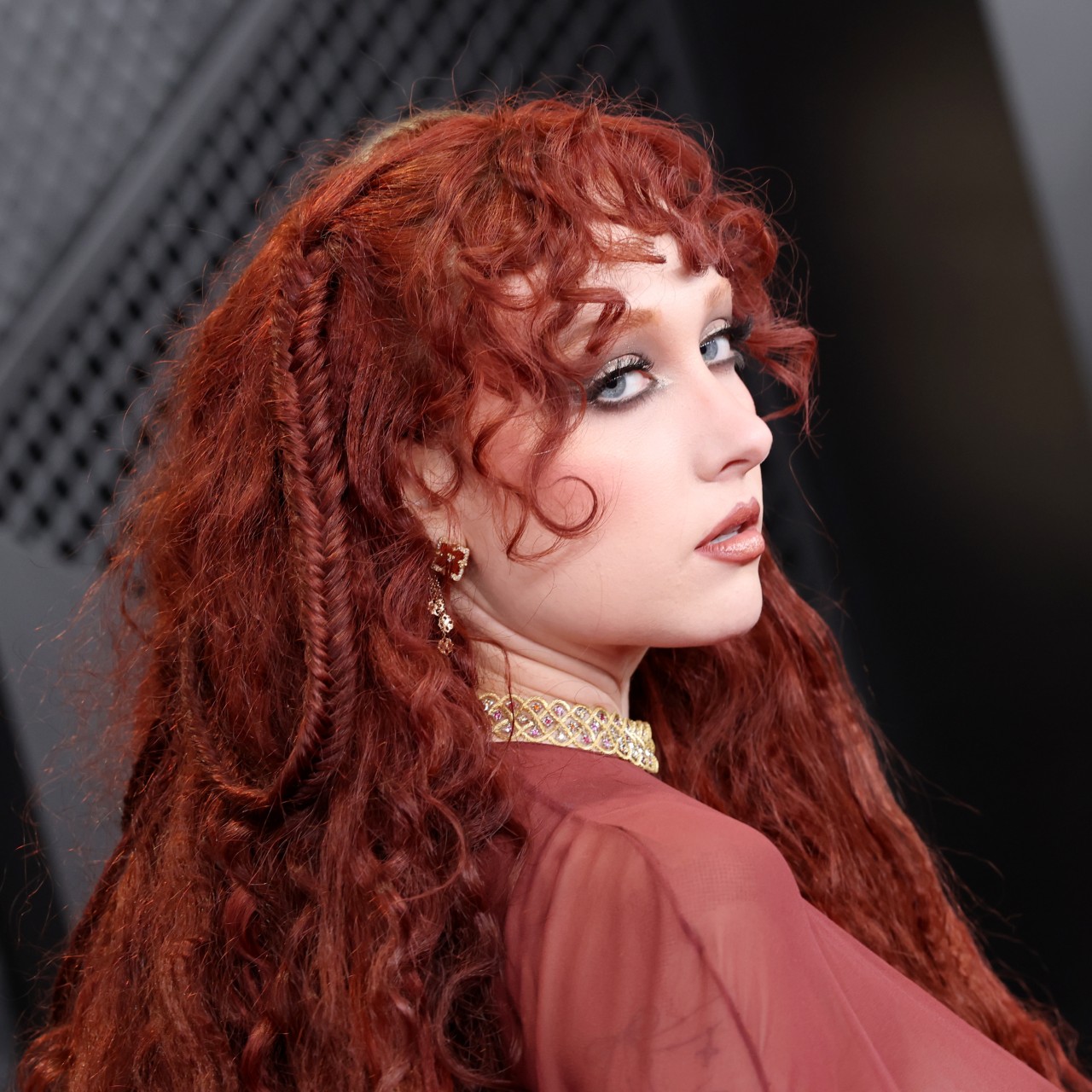 a white woman with curly red hair poses on a red carpet before an awards show