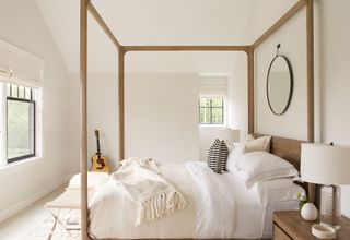 Wooden four posted bed in master bedroom with nightstand and round mirror in space above headboard